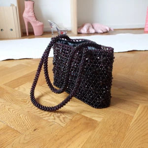 pärlad axelväska - Pärlad liten axelväska i mörklila. dragkedja upptill samt litet fack innuti för plånbok etc. 