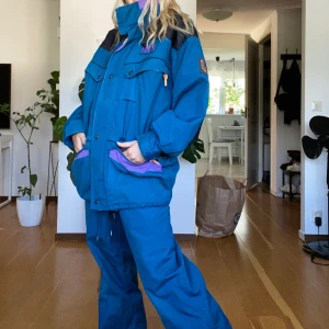 Tuxer retro skidställ  - Säljer mina föräldrars super sköna retro skidställ från Tuxer sport and Adventure.  Dessa ställ har bara hängt i garderoben i flera år och är väldigt välbevarade och hela med tanke på hur gamla dem är.   FÄRG: Mörkblå, lila, svart och gul  Byxorna är med knäpphängslen och två fickor med dragkedja och justerbar resor i midjan. Storlek S. Jackan har fyra fickor, två midjefickor med dragkedja och två bröstfickor med dragkedja samt en bröstficka på insidan (dock trasig dragkedja). Justerbar resor i kragen, midjan och nedtill. Kragen är fodrad och har Invikbar luva. Storlek S. Köparn står för frakten