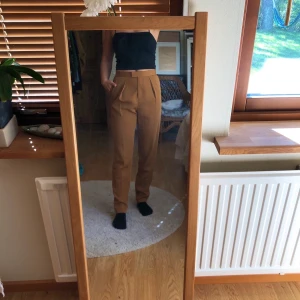 Bruna kostymbyxor - Brun/beiga kostymbyxor i fint skick (färg mest lik bild 1). 2 fickor framtill, en fejkficka baktill. Stängs med både drakbedja, knapp och spänne. Säljs pga att de är aningen för pösiga. 