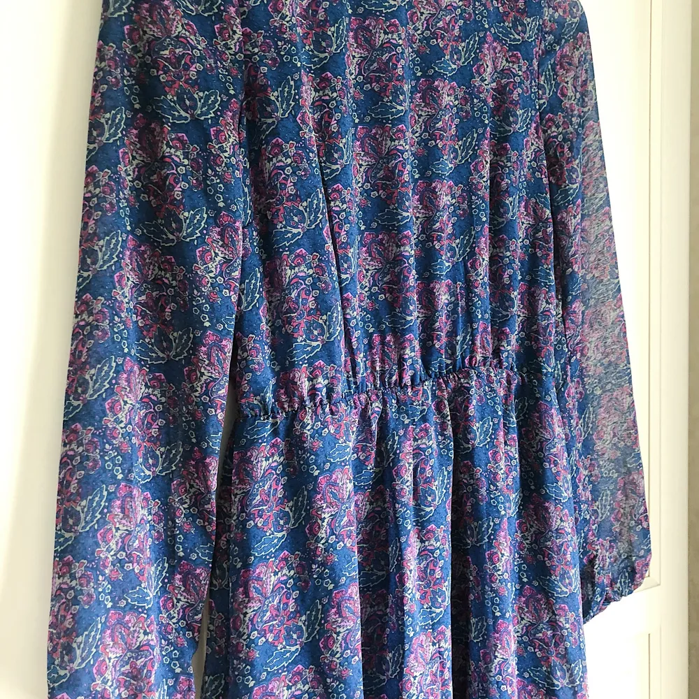 Blommönstrad, blå/lila klänning med öppen rygg, tunna ärmar och guldkedja som accessoar baktill. Från BIKBOK. Passar XS och S.. Klänningar.