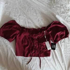 Vinröd topp - Vinröd topp från Nelly. Strl 38 men ingen stretch så jag skulle tro att den snarare passar en 36. Oanvänd med alla lappar kvar, säljes pga för liten. Dragkedja på sidan. Frakt tillkommer 