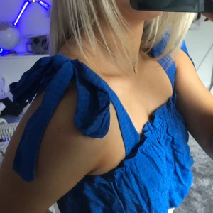 Blått linne med rosetter  - Säljer ett supergulligt blått linne med rosetter som band, det går att bestämma var man vill att rosetterna ska sitta (tex längre bak på ryggen) rosetterna går alltså att knyta upp. Linnets material är vågigt/refligt. Den är aldrig använd !! 💙💙frakt tillkommer