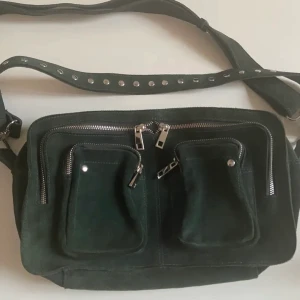 Nunoo väska - Säljer jättefin mörkgrön väska i mocka från danska märket Nunoo i modellen Alimakka! Köpt för 1600 kr på Nelly.com. Väskan är rymlig och nästan helt oanvänd, endast använd 2 gånger!💚💚 hör av er vid frågor