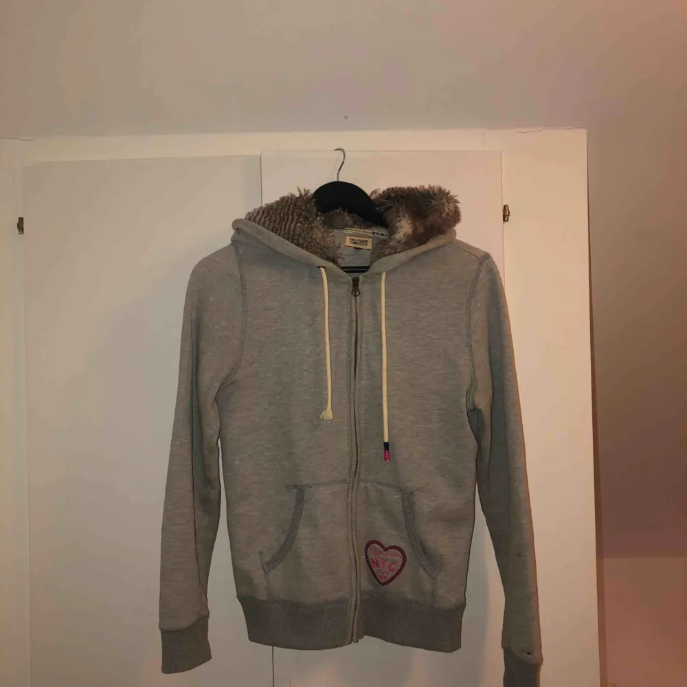 Jättefin hoodie med dragkedja framtill från Hilfiger Denim. Köpt på Tommy Hilfiger i Stockholm för 1300kr. Jätteskön luva med foder (fuskpäls). Jättefint skick, ena snöret är dock skadat (sista bilden) . Hoodies.