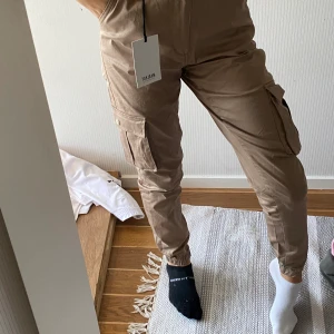 Cargo byxor stl XS - Jag säljer ett par beiga cargo byxor från madlady i storlek XS och för mig är de lite för stora så jag skulle mer säga att det är storlek S, jag har aldrig använt dem, lappen osånt är kvar, ingen skada osv