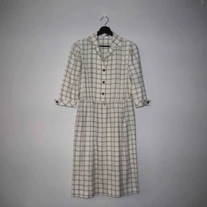  - 70-tals cremevit och brunrutig klänning köpt på en vintage mässa. Tillverkad i USA. Storlek Medium, knälång, tre knappar, tunna axelvaddar och halvlånga ärmar. Llänningen är 114 cm lång, 86 cm i midjan och 46 cm i axelmått. Man kan ha ett bälte i midjan.
