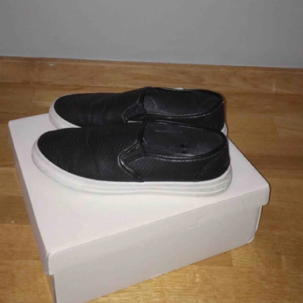 Ett par svarta slip on sneakers i strl 40 från NLY Shoes. Använda endast ett fåtal ggr så de är i extremt fint skick. Nypriset var 200 SEK men jag säljer nu för mer än halva priset. Vid betalning: möts upp, tar endast Swish.. Skor.