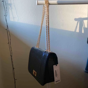 Väska - Svart väska me guld kedja. Aldrig använd ( prislapp finns kvar )   Köparen står för frakten , 