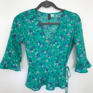 Grön blommig blus - Oanvänd väldigt söt/kvinnlig blus från HM med lite volang nertill. Finns på Kungsholmen eller skickas :) Den är normal upptill - galgen trycker ut sidorna på armen!
