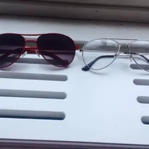 Två par jättesnygga glasögon, den röda är solglasögon med bågar i metall, och den andra är glasögon färgen är silver i pilotmodell med metallbågar. Klarglas.