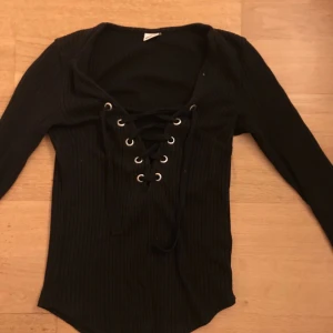 - Svart ribbad tröja med knytning från Gina Tricot. Storlek XS Frakt står köparen för själv. Använd ett antal gånger men i bra skick.