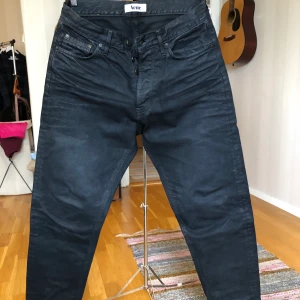 ACNE jeans 32/34 - Svarta jeans från Acne i stl 32/34. Modellen heter Venice och färgen Heavy Black är en djupt svart, nästan vaxad färg. Det gör att jeansen är väldigt svarta trots att de tvättats. Begagnade men i bra skick. 