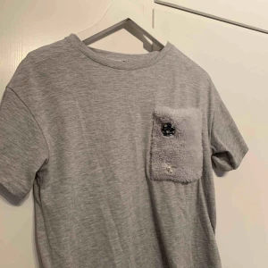  - Grå mysig T-shirt med detaljer på bröstet. 
