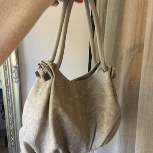 Söt väska - Söt väska i en perfekt modell! Väskan har lite blommigt mönster och är i en fin vit färg materialet är lite läderaktigt. I denna väska får du plats med ganska mycket då den är liten men rymlig! Jag får plats med dator och annat i den❤️