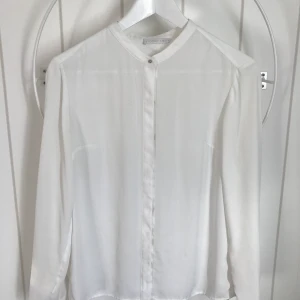 Blus Stockh’LM - Vit blus från märket Stockh’LM. Fin detalj med silverpärlan som knäppning i halsen. Storlek 36. Kan skickas, köpare står själv för frakten.