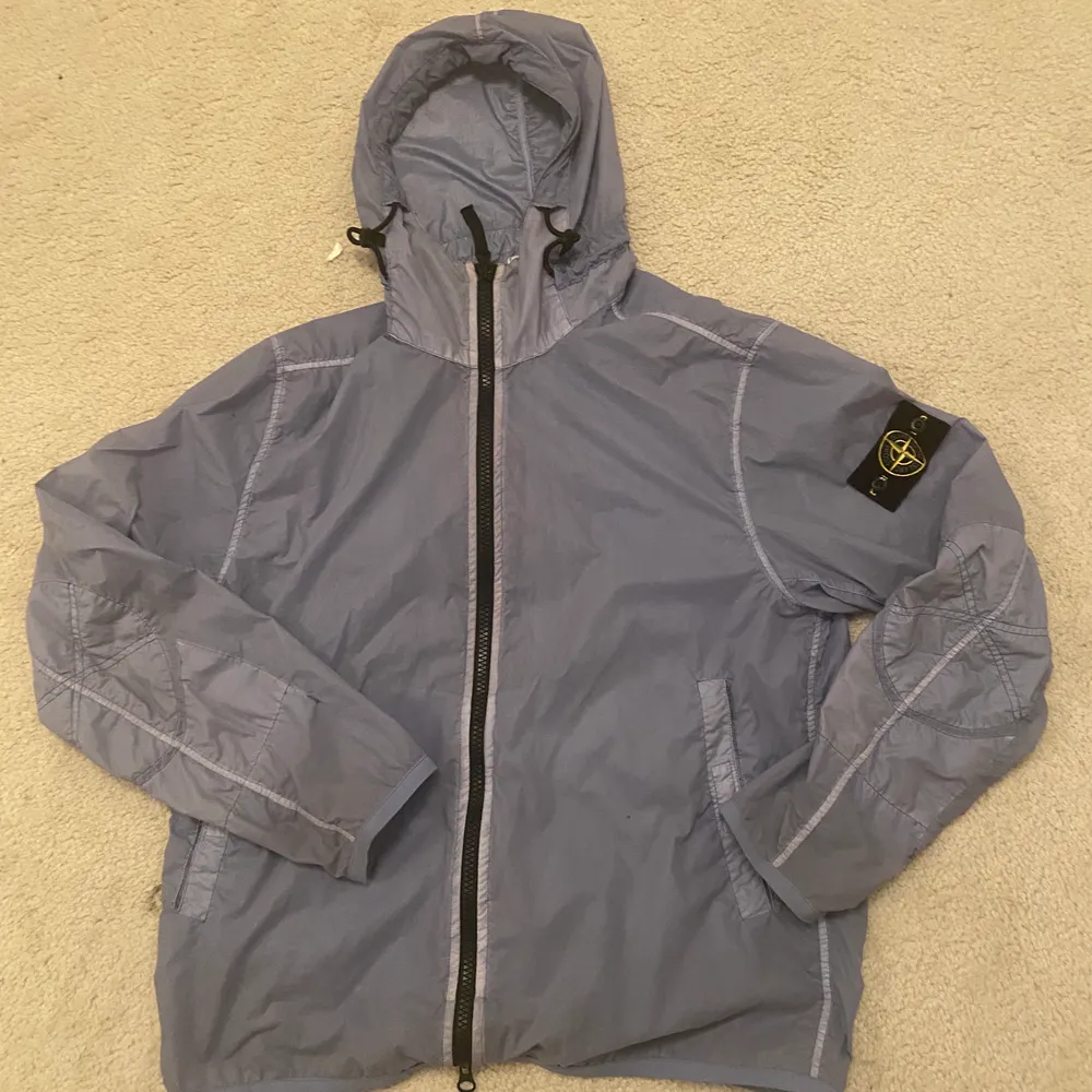 Stone Island wind jacka. Använd fåtal gånger och är i mycket bra skick! Storlek L. Nypris 6000kr. Beskrivning från företaget: Hooded jacket from Stone Island in a garment dyed, wind resistant fabric. This thin nylon jacket closes with a durable two-way zipper and the hood is adjustable. The front has two slant pockets with concealed zippers and the sleeve ends and hem have elastic taping keeping the wind out. The classic, removable Compass patch is placed on the left upper sleeve. Closes with two-way zipper Wind resistant Water repellent fabric . Jackor.
