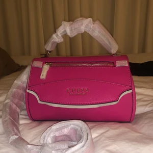 Guess väska  - Äkta Rosa Guess väska med gulddetaljer, helt ny med plast och prislapp på.                                 Måtten är: 10.5"W x 6.75"H x 4"D 💗              Modellen heter- Lias top handle flap                    Skriv för mer info/bilder!   