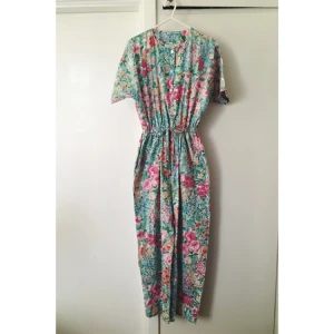  - Fin somrig byxdress med blommigt mönster. Kortärm och resår med snöre i midjan. Knappar hela vägen. 