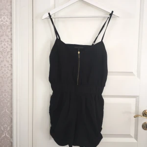  - Svart shortsdress med guldig dragkedja, reglerbar axelband, fickor på sidorna. 