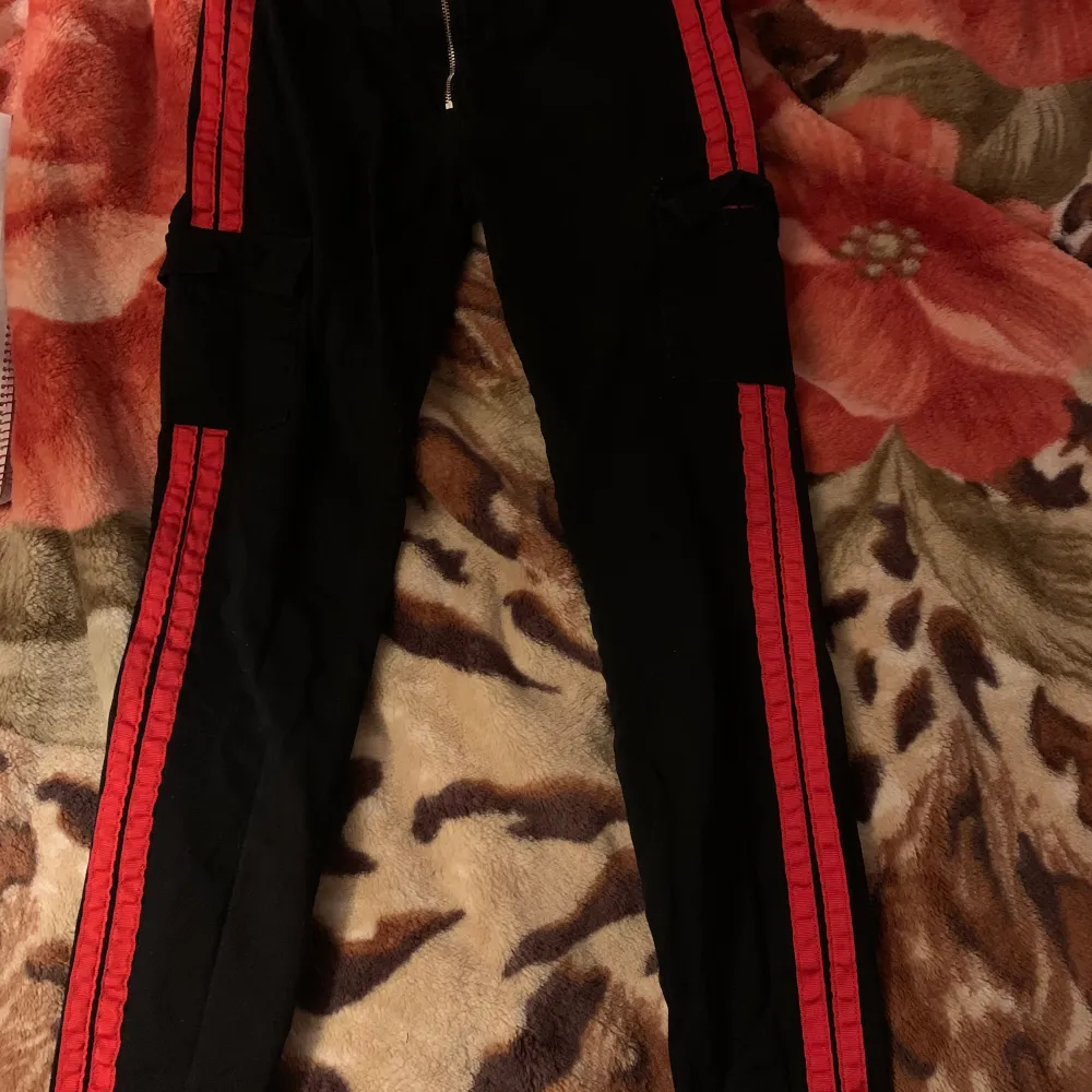 Svarta byxor med röda sträck på sidorna. Har 2 fickor fram och 2 fickor på sidorna. Jeans liknande material. Storlek S. Jeans & Byxor.