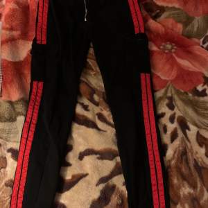 Svarta byxor med röda sträck på sidorna. Har 2 fickor fram och 2 fickor på sidorna. Jeans liknande material. Storlek S