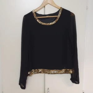 Svart blus strl 40 - Svart festlig blus med guld paljetter, från Gina Tricot.