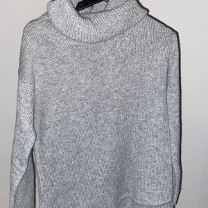 Grå stickad tröja - Grå stickad tröja från Ellos. Storlek 34, men passar mig som brukar bära storlek S. Använd fåtal gånger. Kragen är vikbar därför ligger den lite konstigt på bilden då galgen inte gjorde det rättvisa. 😊