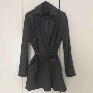  - Halvlång gråblå kappa/jacka. Tunn, använts under vår och sommar. Fäster med en knapp framtill, ingen dragkedja. Två fickor. Tygband i midjan. Kan mötas upp i Malmö eller Lund, annars tillkommer frakt på 72 kr.