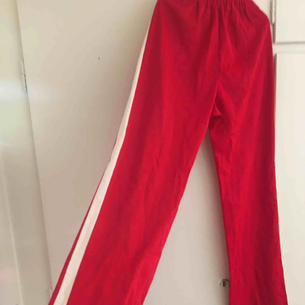 Röda vintage trackpants med vit rand på sidorna. Lätt utsvängda i benen. Troligen hemmasydda för finns inget märke i dem, men de är väldigt välsydda i bra kvalite och har fina detaljer som ”kostymveck” på benen, se bild 2. Resår i midjan. . Jeans & Byxor.