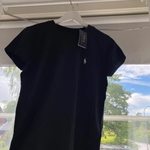 Ralph Lauren tshirt - En oanvänd Ralph Lauren tshirt i storlek S. En mörkblå/gråaktig färg med en vit häst. Aldrig använd, lappen finns kvar. 150kr