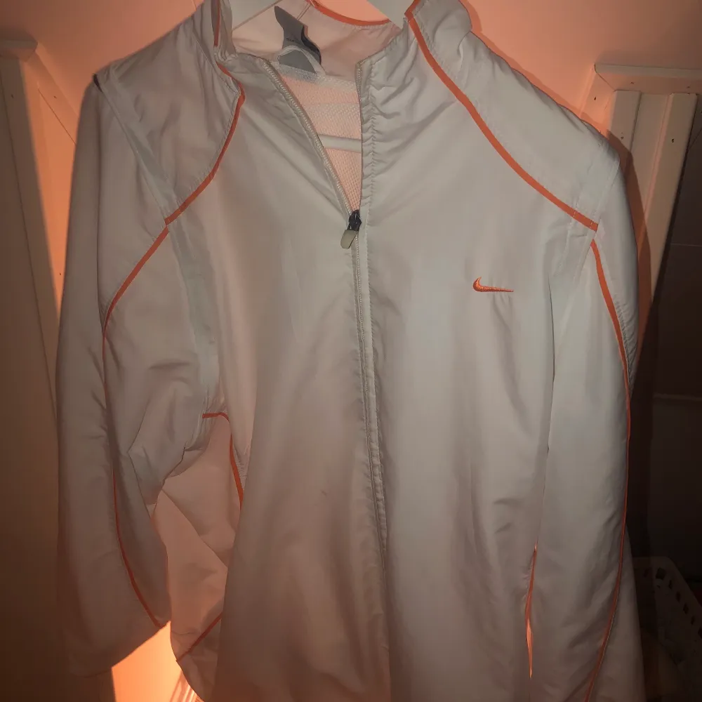 En vit sportjacka från Nike med orangea ränder. Jätte cool och väldigt bra skick. Frakt TILLKOMMER!. Jackor.