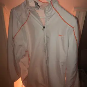 En vit sportjacka från Nike med orangea ränder. Jätte cool och väldigt bra skick. Frakt TILLKOMMER!
