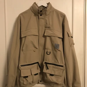 Carhartt Elmwood jacka - Jacka från carhartt i beige med 11 fickor inkl. Innerficka. Har luva. Skick 8/10. Nypris: 2400kr. Pris kan diskuteras vid snabb affär. DM för fler bilder🤙🏻