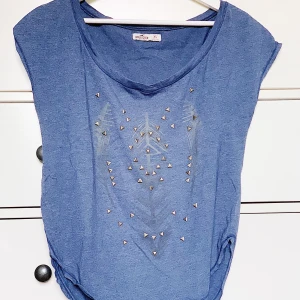 Detaljerad T-shirt!  - Supersnygg V-ringad T-shirt från Hollister. Kan användas som off shoulder. Coolt tryck med stenar. Knappt använd! Slits på båda sidorna, alltså enkelt att ha innanför byxorna utan att de syns. Pris kan diskuteras & köparen står för frakt! 💙