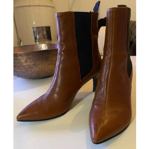 Vagabond Boots Whitney  - Boots Whitney från Vagabond i stilren modell med spetsig tå och högt skaft med kontrastfärgad resår på båda sidor. Klädd klack. Gjorda i fint, blankt skinn med textilfoder och skinninnersula. Skafthöjd 14 cm, klackhöjd 8 cm. Nypris 1300kr 
