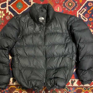 The north face dunjacka  - Black North Face 700 down dunjacka. Retro nuptse. Jackan är använd men skicket är fortfarande bra! Finns två gummiband längst ner på jackan som man kan dra åt! Frakt tillkommer! 700kr eller bud!
