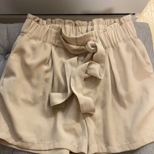 Shots  - Kostym shorts med snöre och detalj runt midjan. Färgen beige. 