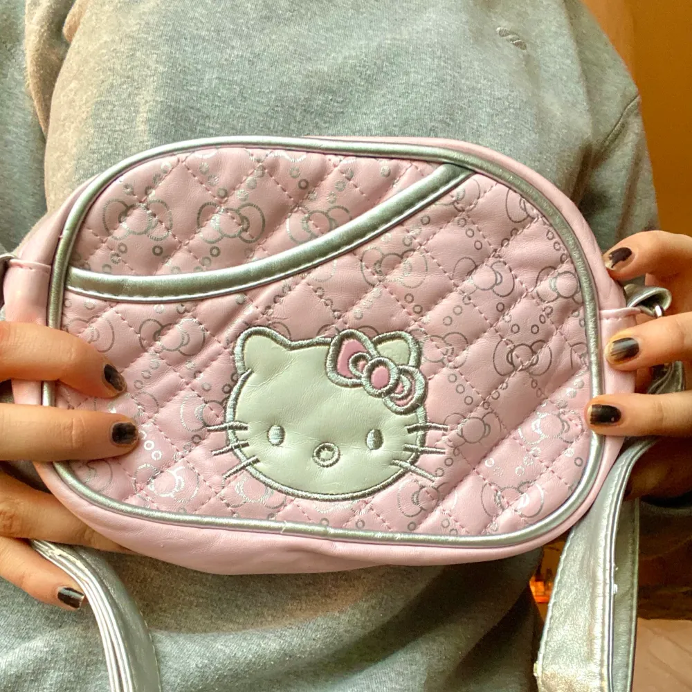 Justerbar Hello Kitty handväska! Ljusrosa med hello Kittys ansikte på ena sidan och ett justerbart silvrigt band! Köpt second hand, använt skick (små slitningar här och där på axelbandet). Frakt 22kr  . Väskor.