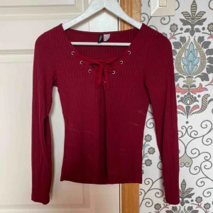  - Röd tröja med snörning vid bröstet.