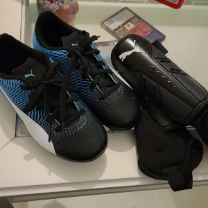 Puma fotbollsskor samt Puma benskydd  - För spel på gräs, ovandel i syntetmatrial, snörning för bra passform. Softfoam-innersula för extra komfort. Skor strl:31 NYPRIS:600:-                                   Benskydd strl:XS  NYPRIS:200  FRAKT TILLKOMMER