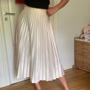 Plisserad kjol - Champagnefärgad plisserad kjol i satin. Bra skick. Bekväm och användbar till både vardag och fest. 