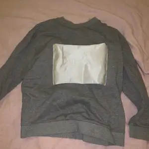 En grå tröja som har en vit tyg bit på framsidan 