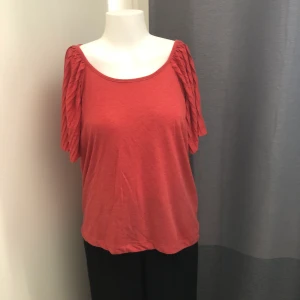 T-shirt med plisserade ärmar - Fin korallröd T-shirt från Rules by Mary med plisserade vida ärmar. Sparsamt använd. Storlek S
