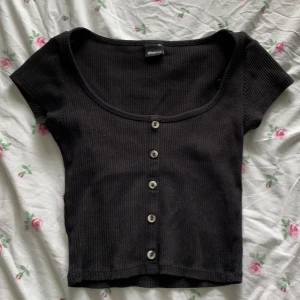 Svart T-shirt - Svart t-shirt med små knappar, urringning, mer åt magtröja än t-shirt, storlek Xs köparen står för frakten