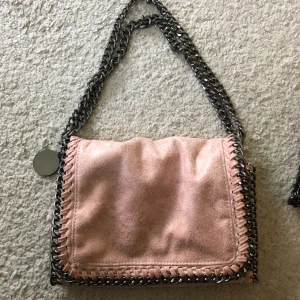 Trendig väska - Rosa väska. Oanvänd så i nyskick. Lite sådär blankt material. Egentligen är det långa band men man kan (som på bilden) fixa så att de blir kortare🥰