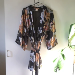  - Superfin kimono med blommigt mönster. Tyget är mörkgrått transparent där det inte är blommor. Har använt den med bara bh under utan att känna mig "naken". Använd några få gånger, och i nyskick. 50% viskos, 50% polyester. Frakten ingår i priset. Nypris var 500kr. 