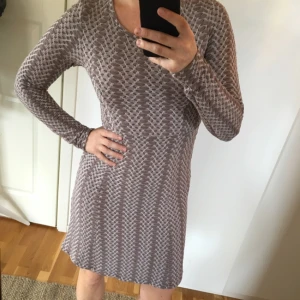  - Grå/beige klänning i böljande tyg med struktur. Stretch. Avskuren i midjan och lätt klockad kjol.