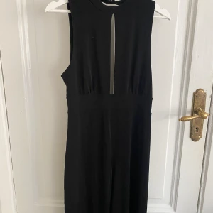 Svart Byxdress - Svart byxdress med långa halvt utsvängda ben. Öppen i ryggen och en liten slits vid bysten. Möts på Södermalm och vid frakt står köparen för kostnad!