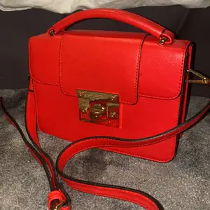Röd väska med guldiga detaljer från Lindex! Väskan är i super bra skick och sparsamt använd. Det är ett stort fack och ett mindre innerfack. Väskan har en axelrem men även ett trendigt litet handtag uppepå!