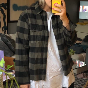 Rutig Skjorta / Flanell - Grön/svart flanellskjorta med avklipp kant. Kortare framtill än bak och slits på sidan. 